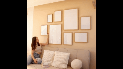 Multiple Wall Art Frame Mockup- a girl sitting on a couch while reading and her background is multiple different sizes of frames
